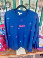 A navy blue crewneck sweatshirt with small embroidered fish motifs and 'Buffalo' text on the chest, hanging on a black hanger on a wooden table.