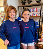 An older woman and a young girl wearing matching navy blue sweatshirts with a red 'Buffalo "go and small red and white embroidered details, standing in a retail store.